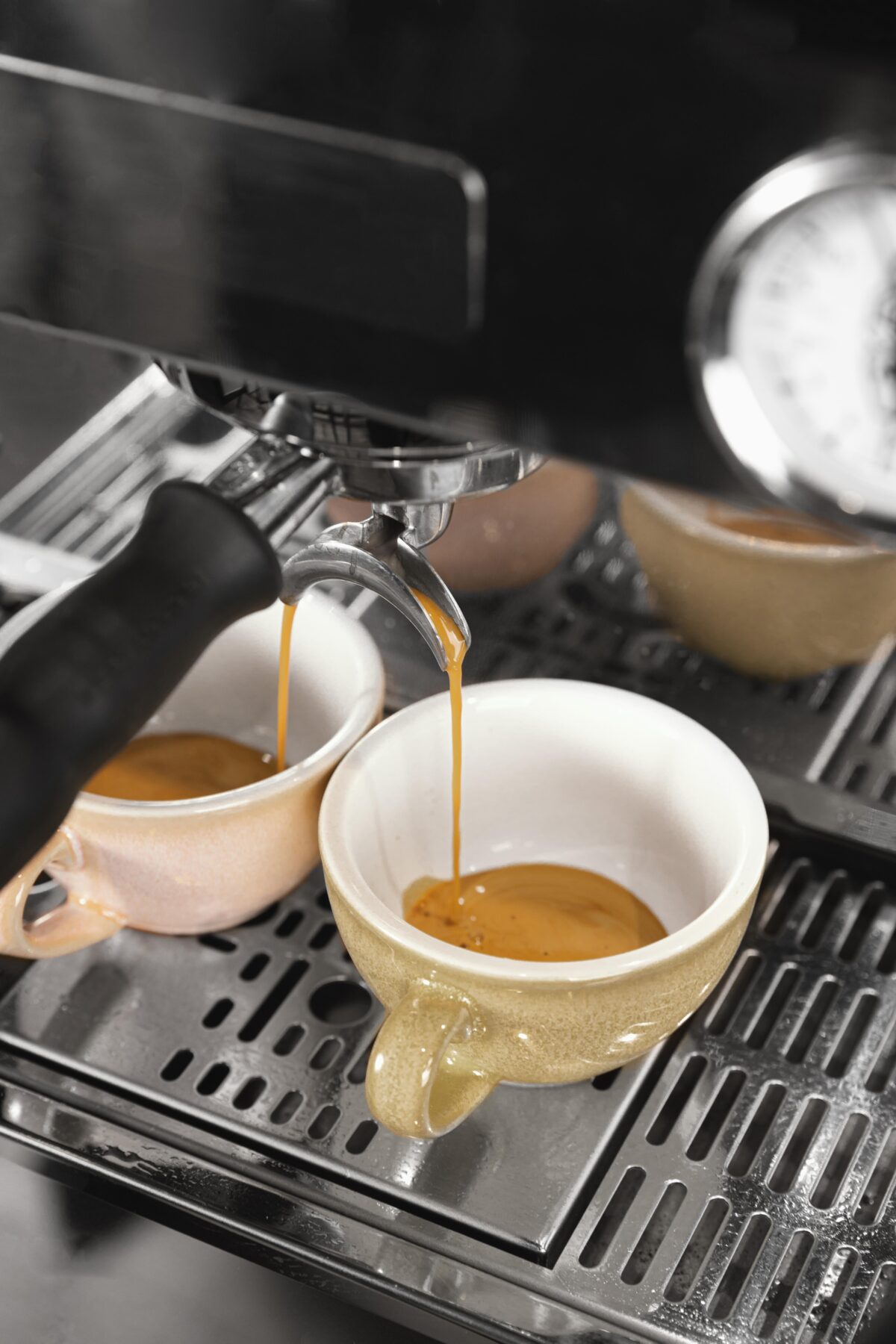 Vers gezette espresso stroomt uit een professionele espressomachine in twee keramische kopjes, een voorbeeld van cafeïnegehalte in koffie.
